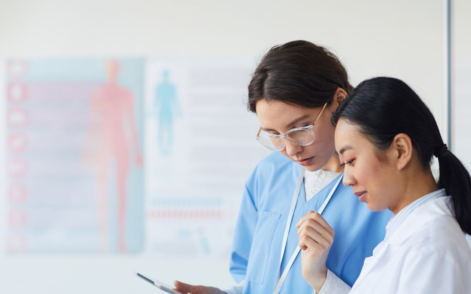 Side view portrait of two female medics writing on clipboard while standing in medical office interior, copy space